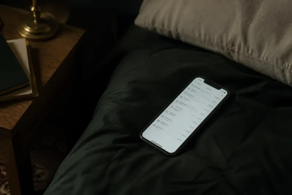 Celular boca arriba en una cama a oscuras, con la pantalla de un extracto bancario encendida.
