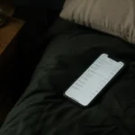 Celular boca arriba en una cama a oscuras, con la pantalla de un extracto bancario encendida.