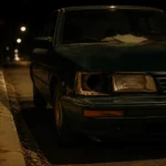 Auto detenido al costado de una avenida de noche, faro roto y papeles sobre el tablero